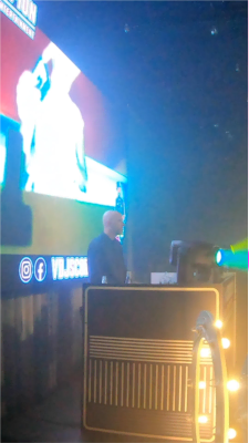 Ein Video-DJ steht vor einer großen Leinwand hinter seinem DJ-Pult.