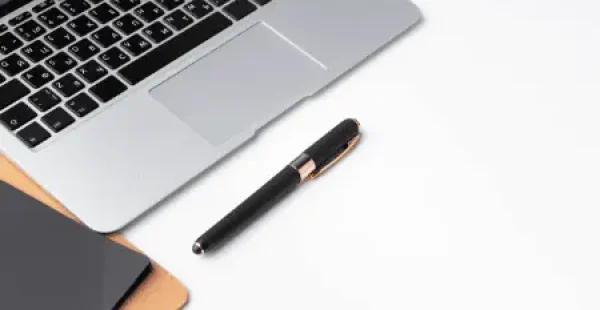 Ein Laptop, ein Stift und ein Notizbuch auf einer weißen Oberfläche.